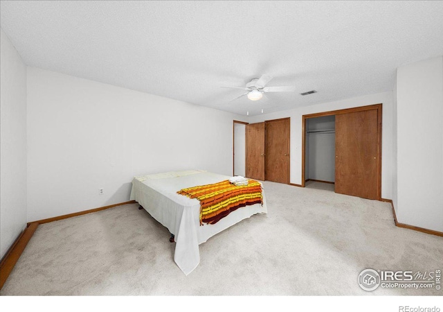 bedroom with multiple closets, visible vents, light carpet, and baseboards