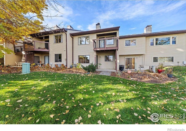 rear view of property with a balcony, a chimney, central AC, and a yard