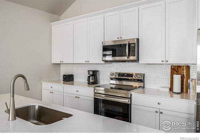 kitchen with sink, stainless steel appliances, tasteful backsplash, lofted ceiling, and white cabinets