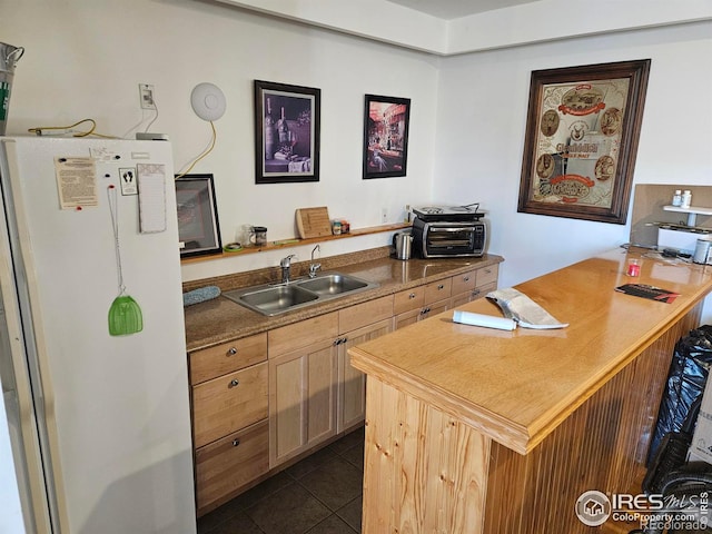 kitchen with light brown cabinets, white fridge, dark tile patterned floors, and sink