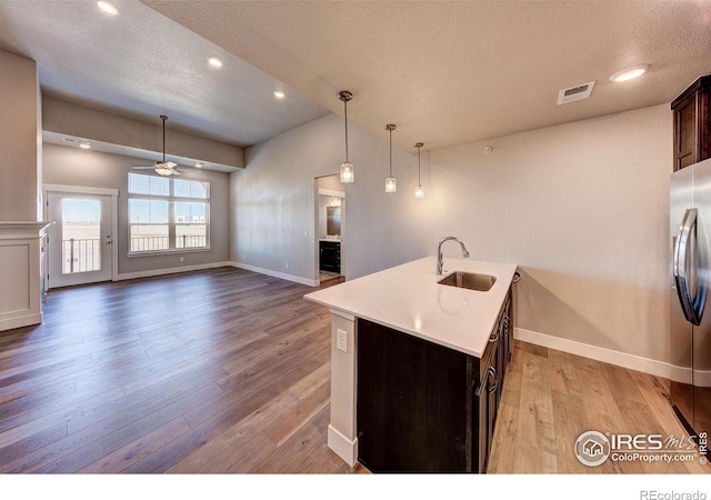 kitchen with dark brown cabinetry, sink, stainless steel refrigerator with ice dispenser, an island with sink, and light hardwood / wood-style floors