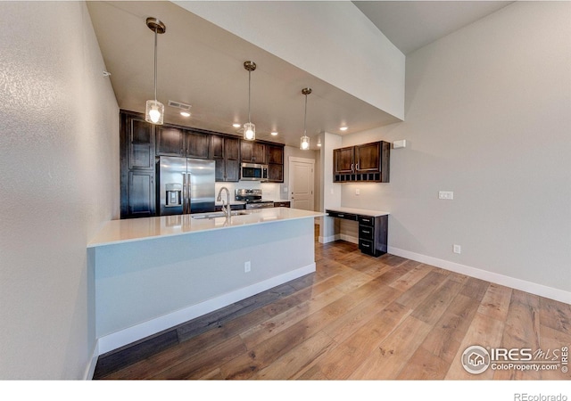 kitchen with appliances with stainless steel finishes, dark brown cabinets, sink, hardwood / wood-style floors, and hanging light fixtures