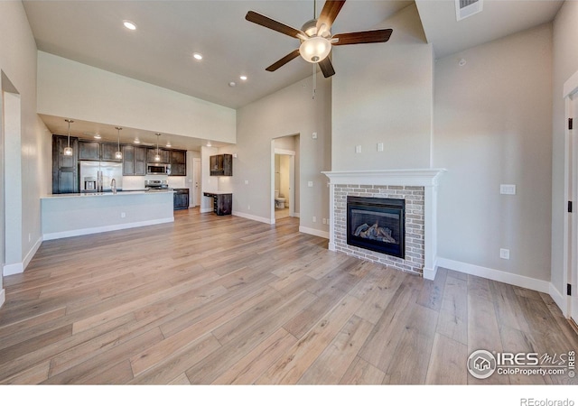 unfurnished living room with light wood-type flooring, high vaulted ceiling, and a brick fireplace