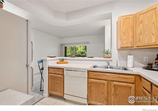 kitchen featuring light brown cabinets, a peninsula, white appliances, a sink, and light countertops