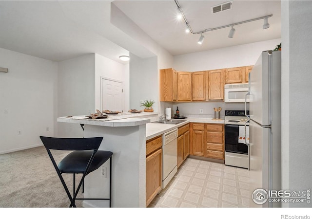 kitchen with white appliances, a breakfast bar area, a peninsula, light countertops, and a sink