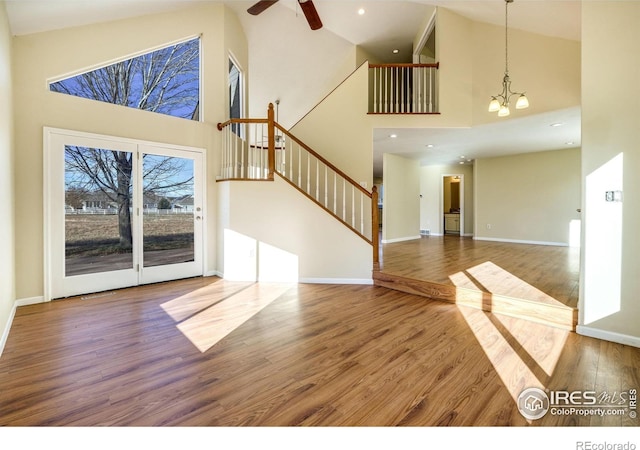 unfurnished living room with high vaulted ceiling, wood-type flooring, and ceiling fan with notable chandelier