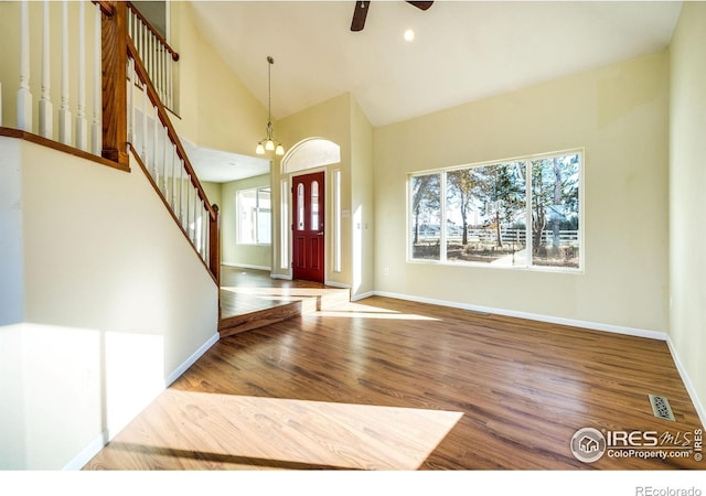 foyer entrance with high vaulted ceiling, wood-type flooring, and ceiling fan with notable chandelier