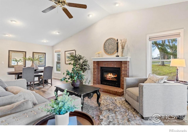 living room with ceiling fan, light hardwood / wood-style floors, lofted ceiling, and a fireplace