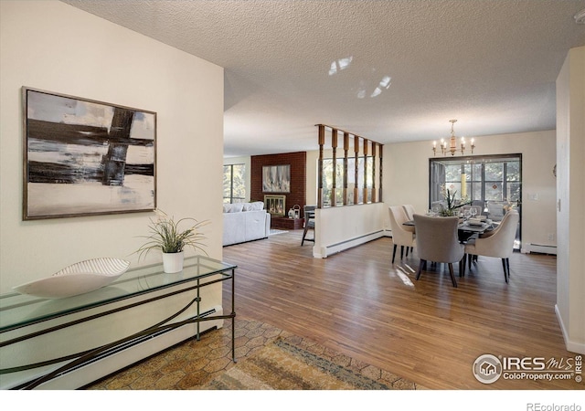 dining space featuring an inviting chandelier, a baseboard heating unit, wood-type flooring, a textured ceiling, and a fireplace