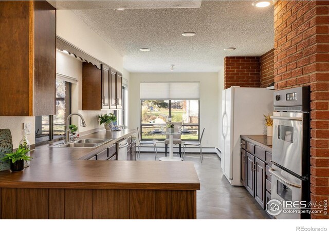 kitchen with sink, stainless steel appliances, brick wall, kitchen peninsula, and a textured ceiling