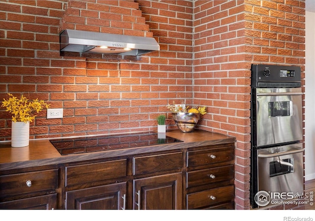 kitchen with dark brown cabinets, ventilation hood, double oven, and brick wall