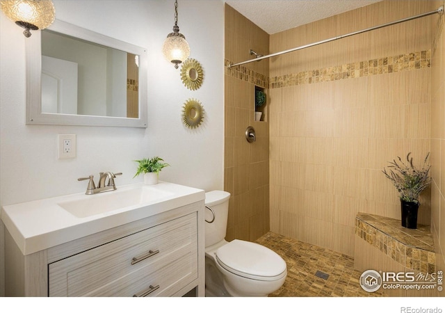 bathroom with a tile shower, vanity, a textured ceiling, and toilet