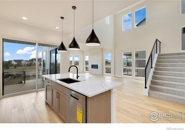 kitchen featuring light stone countertops, sink, light hardwood / wood-style flooring, stainless steel dishwasher, and pendant lighting