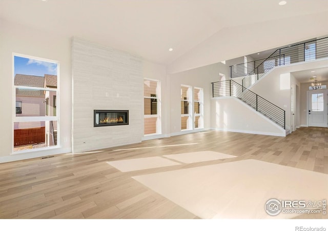 unfurnished living room featuring a tile fireplace, hardwood / wood-style floors, a chandelier, and high vaulted ceiling