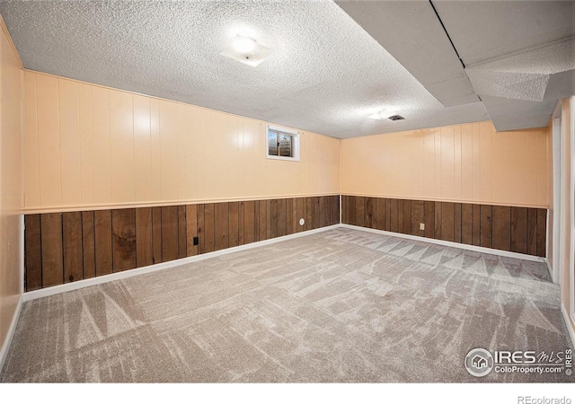 basement featuring carpet flooring, a textured ceiling, and wood walls