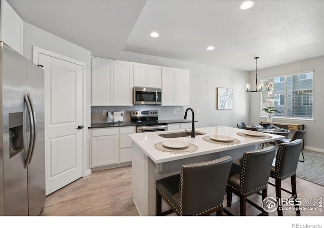 kitchen featuring a kitchen island with sink, sink, light hardwood / wood-style flooring, decorative light fixtures, and stainless steel appliances