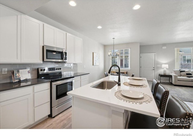 kitchen with a breakfast bar, hanging light fixtures, sink, an island with sink, and appliances with stainless steel finishes