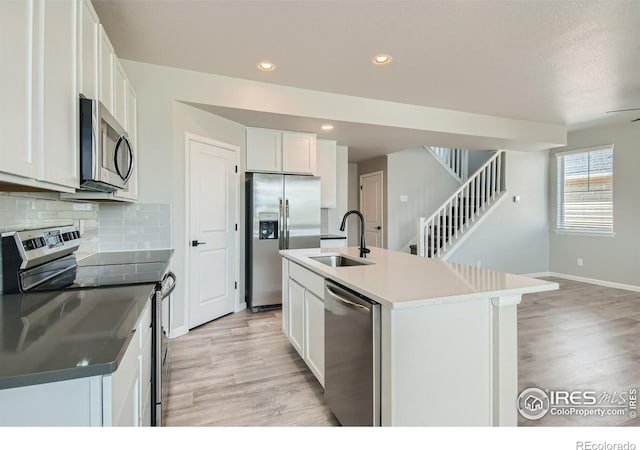 kitchen featuring appliances with stainless steel finishes, light wood-type flooring, sink, white cabinets, and an island with sink