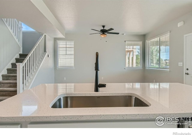 kitchen featuring light stone counters, sink, ceiling fan, and a textured ceiling