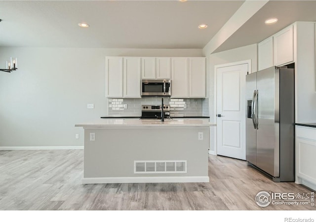 kitchen featuring stainless steel appliances, white cabinetry, light hardwood / wood-style floors, and an island with sink