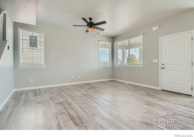 empty room with a textured ceiling, light hardwood / wood-style flooring, plenty of natural light, and ceiling fan