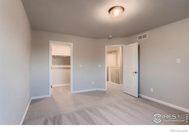 unfurnished bedroom with a spacious closet, a closet, light carpet, and a textured ceiling