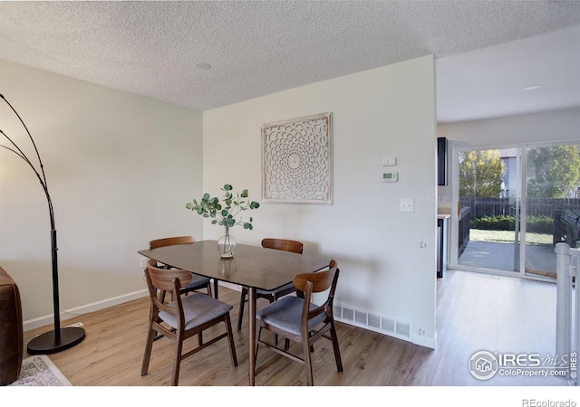 dining space with a textured ceiling and light hardwood / wood-style flooring