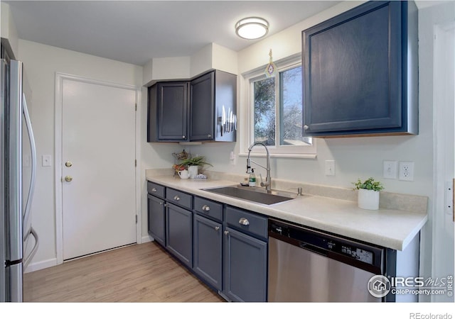 kitchen with blue cabinetry, light wood-type flooring, stainless steel appliances, and sink