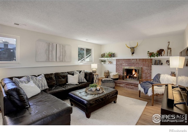 living room featuring wood-type flooring, a textured ceiling, and a brick fireplace