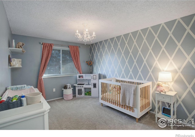 bedroom featuring a crib, a textured ceiling, carpet floors, and a notable chandelier