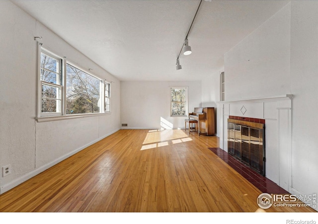 unfurnished living room with light wood-type flooring, a textured ceiling, a tile fireplace, and track lighting