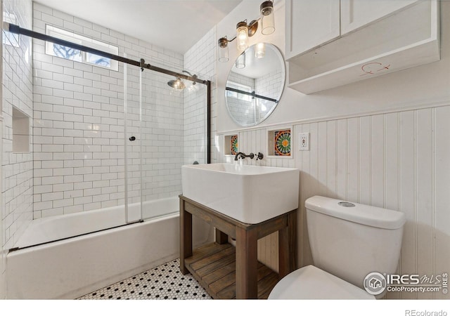 bathroom with wooden walls, bath / shower combo with glass door, and toilet