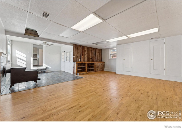 interior space featuring a drop ceiling, light hardwood / wood-style floors, ceiling fan, and wooden walls