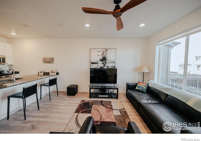 living room featuring light wood-type flooring, ceiling fan, and sink