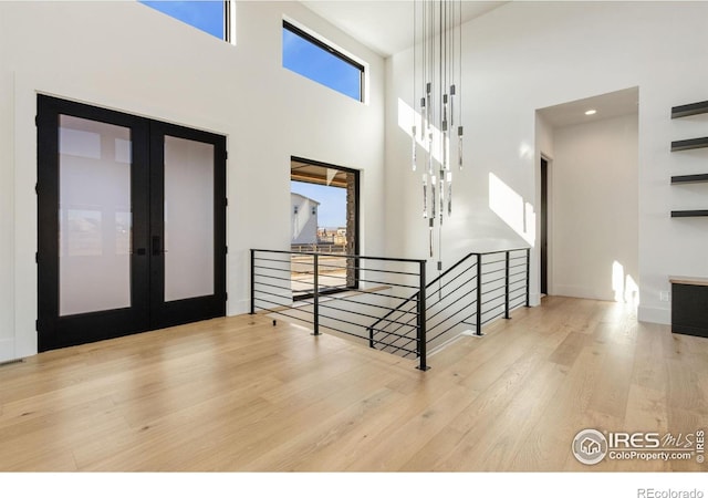 entryway featuring light wood-type flooring, french doors, and a towering ceiling