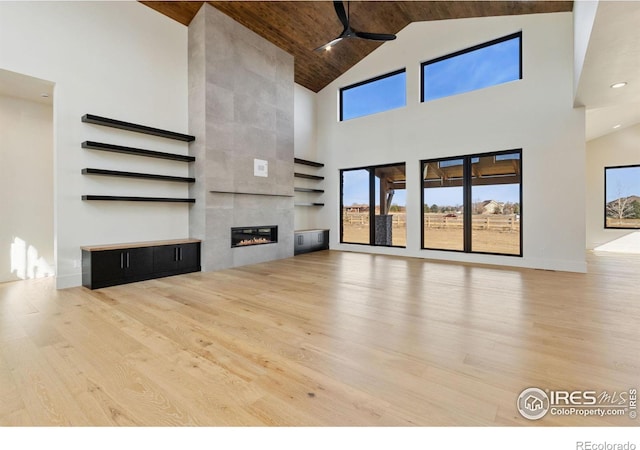 unfurnished living room featuring wooden ceiling, light wood-type flooring, high vaulted ceiling, and a tiled fireplace