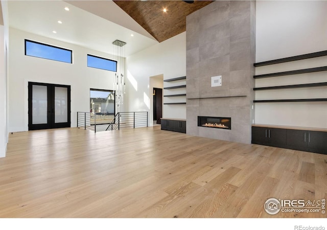 unfurnished living room featuring a tile fireplace, high vaulted ceiling, and light wood-type flooring