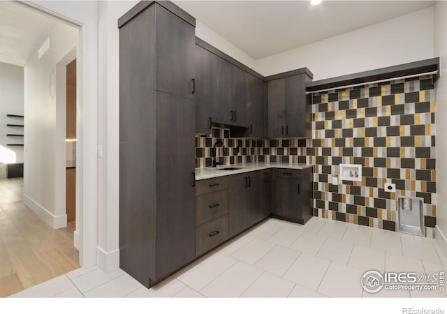 kitchen with decorative backsplash, dark brown cabinets, light hardwood / wood-style flooring, and sink