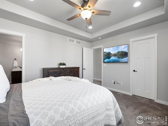 carpeted bedroom featuring ceiling fan, a raised ceiling, and ensuite bathroom