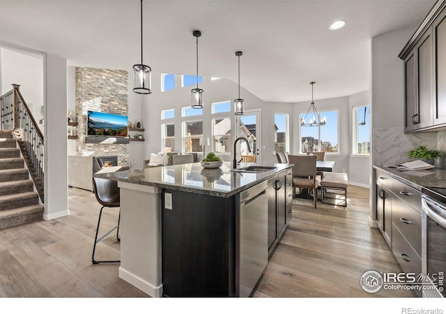 kitchen featuring decorative backsplash, stainless steel dishwasher, sink, a center island with sink, and a fireplace