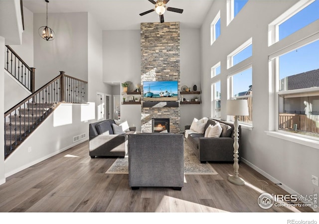 living room with dark hardwood / wood-style floors, ceiling fan with notable chandelier, a fireplace, and a high ceiling