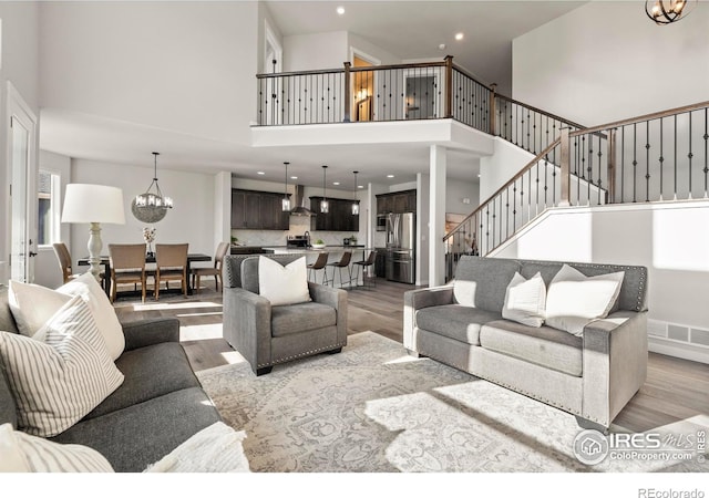 living room featuring a towering ceiling, light hardwood / wood-style floors, and an inviting chandelier