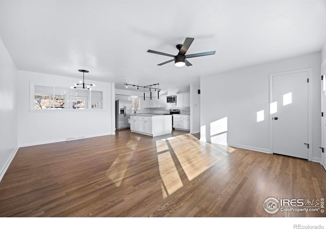 unfurnished living room with hardwood / wood-style floors, rail lighting, and ceiling fan with notable chandelier