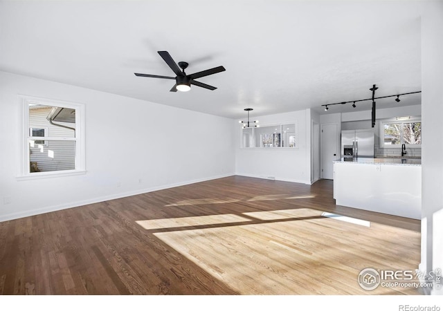 unfurnished living room with ceiling fan with notable chandelier, wood-type flooring, sink, and track lighting