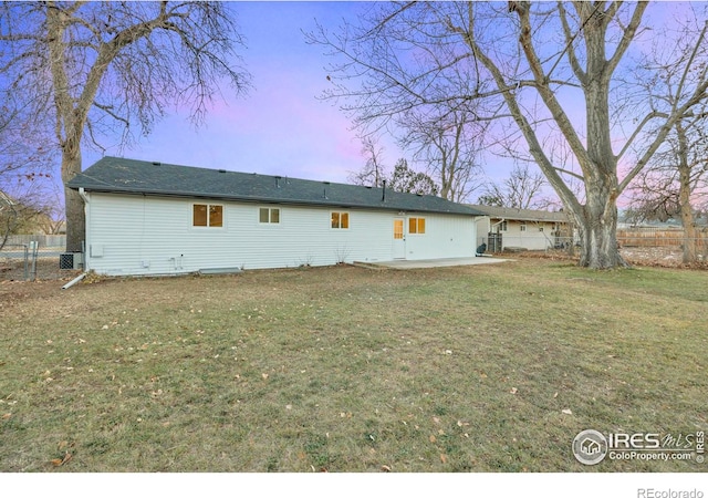 back house at dusk with a yard, a patio, and central air condition unit