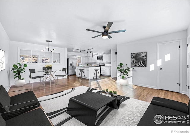 living room with ceiling fan with notable chandelier, light hardwood / wood-style floors, and track lighting