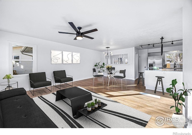 living room featuring sink, rail lighting, wood-type flooring, and ceiling fan with notable chandelier