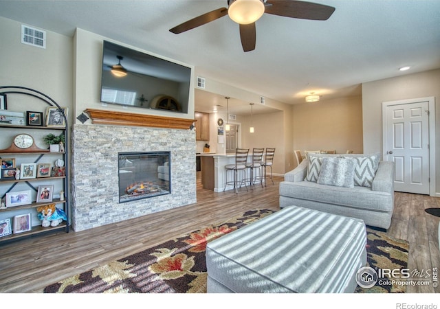 living room featuring ceiling fan, a stone fireplace, and wood-type flooring