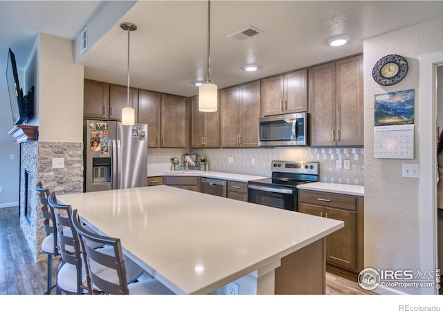 kitchen featuring stainless steel appliances, tasteful backsplash, pendant lighting, wood-type flooring, and a breakfast bar