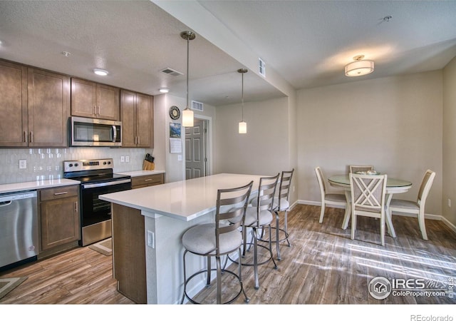 kitchen with a center island, hanging light fixtures, stainless steel appliances, dark hardwood / wood-style floors, and a kitchen bar